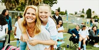 Mother and daughter smiling and playing at an outdoor community event.