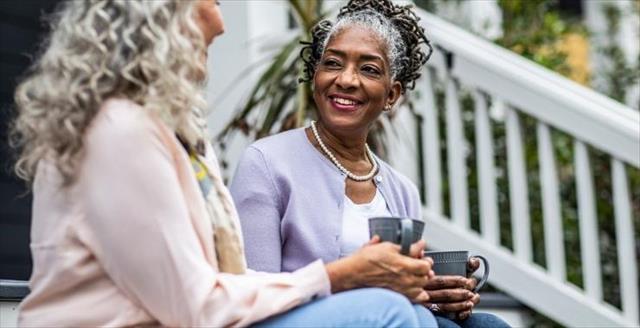 Two women seated on the porch, drinking coffee.