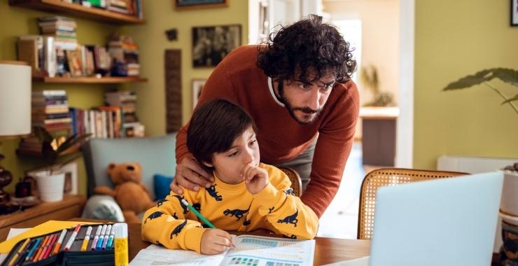 Father helping his son to with schoolwork in front of the laptop at home.