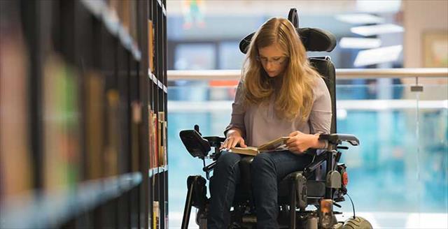 young woman in wheelchair looking at a book in the library