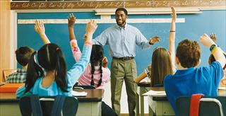 Black male teacher standing in front of a class of elementary school students raising their hands