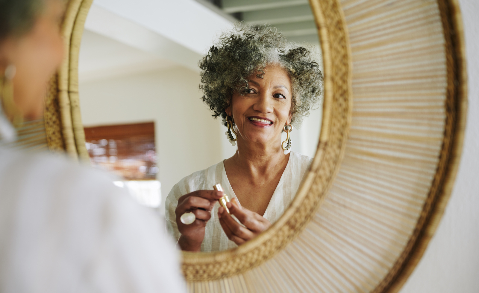 Smiling mature woman putting on lipstick in a mirror at home
