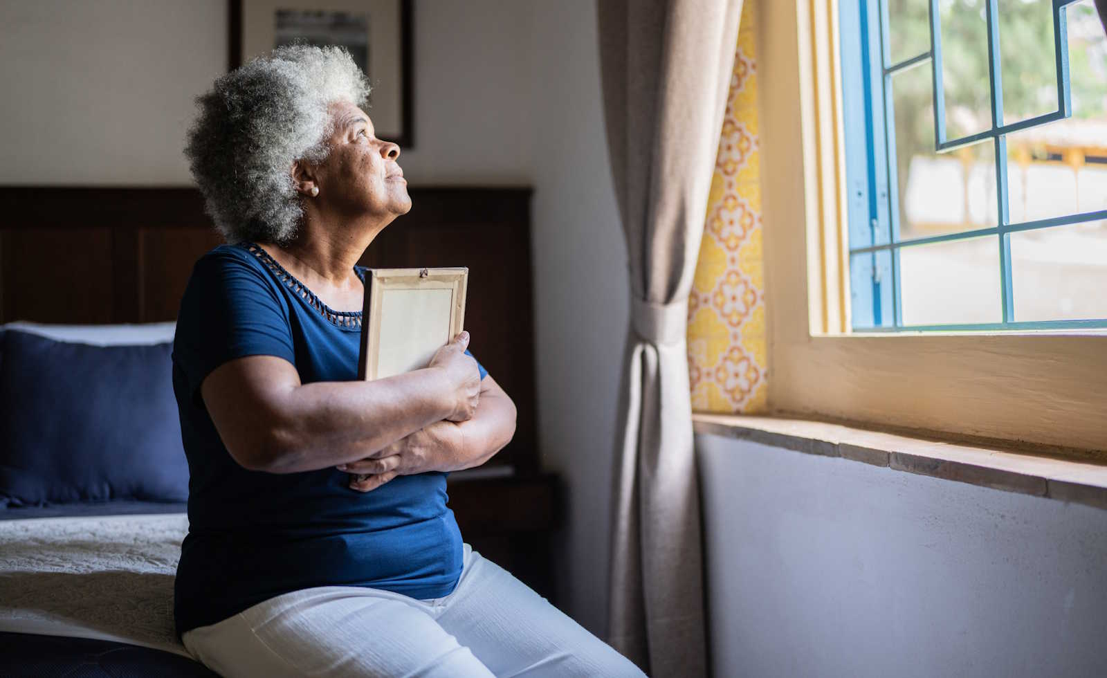 Senior woman holding a picture frame missing someone at home