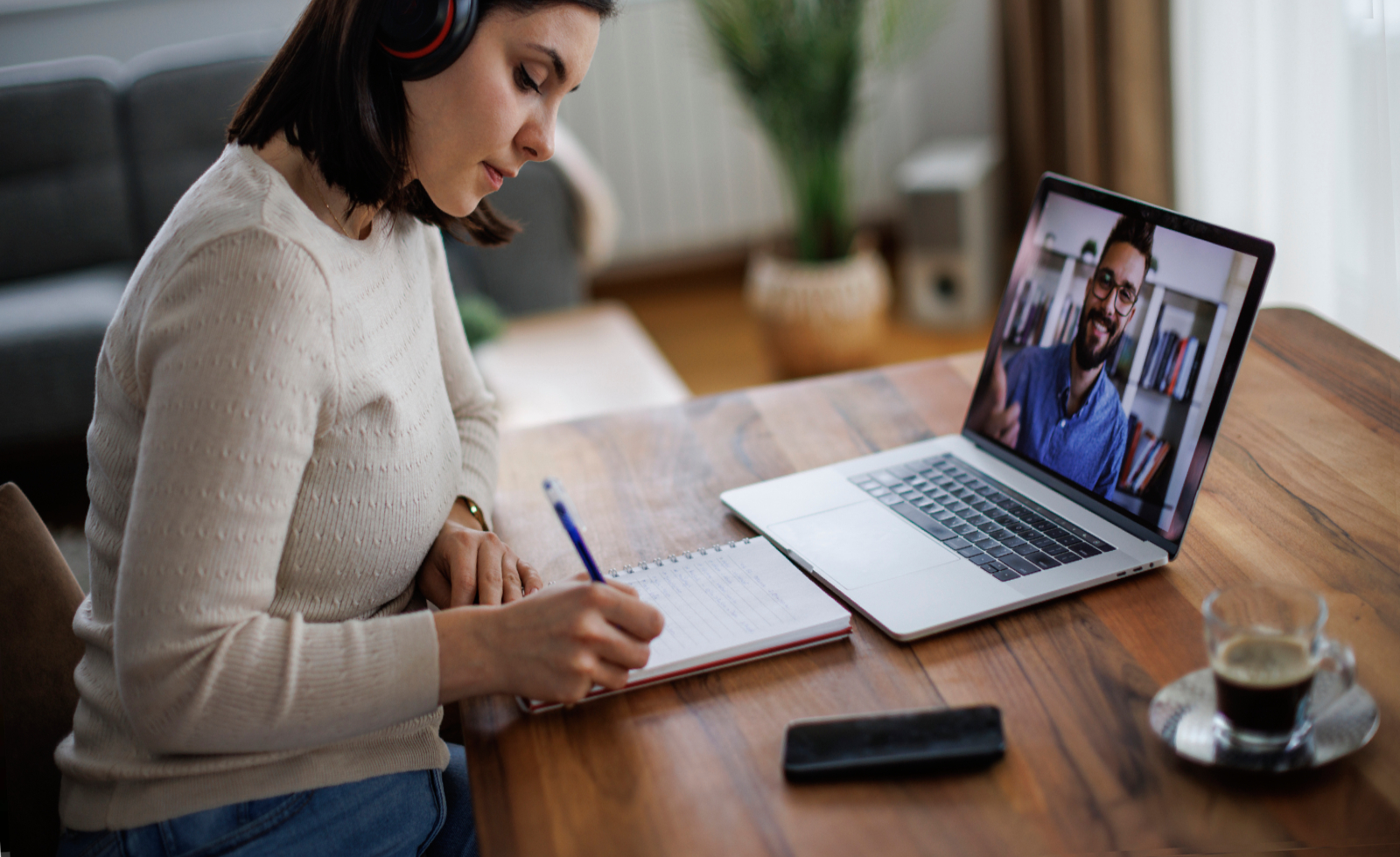 Young woman in headphones attending an online course and making notes