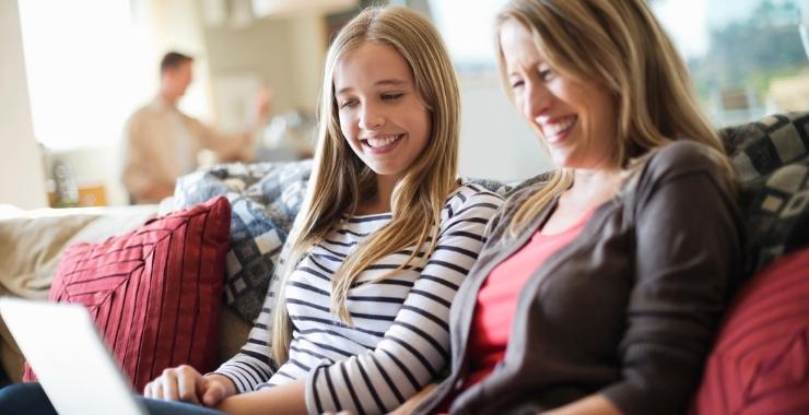 Mother with high school age daughter learning from a laptop and smiling at home.