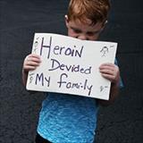 Young boy holding sign reading “heroin divided my family”