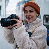 Young woman wearing an orange beanie holding a camera.