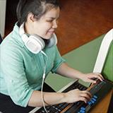 Young, blind student using a computer while sitting at a desk with headphones around her neck.