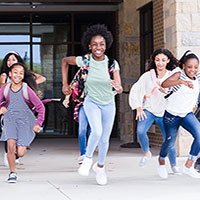 Diverse group of children bursting through the school doors to leave for the day.