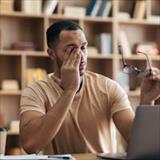 young man rubbing his eyes after looking at his laptop