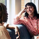 Two people sit facing each other, with one person smiling while engaged in conversation.
