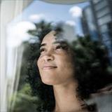 A woman gazes peacefully out of a window, with reflections of trees and sky visible in the glass