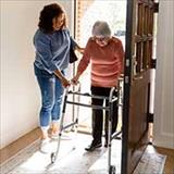 A caregiver assisting an elderly woman with a walker inside her home