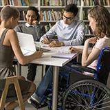 Group of college students, including one student in a wheelchair, sit together in the library.