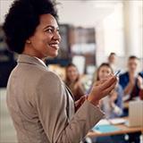 African American female college professor points towards chalkboard in classroom.
