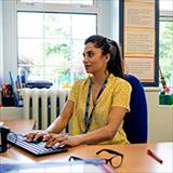 Teacher at desk typing on computer.