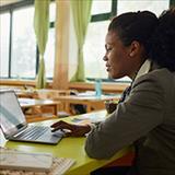Young, African American teacher using laptop in classroom.
