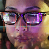 close up of a woman's face with reflection of scientific graphs in her glasses