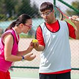 Two young individuals with neurodevelopmental disabilities playing tennis outside.