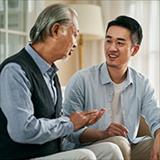Asian elderly father and adult son chatting at home