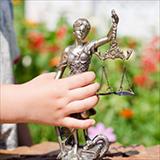 Kid's hand holding sculpture of themis, femida or justice goddess on green leaves natural bokeh background