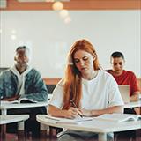 College students seated at desks in classroom; some writing in notebooks, others looking towards the front of the class.