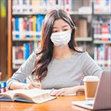 Asian young student wearing surgical mask and doing homework and using laptop in library