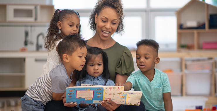 Teacher reads while four students gather around her.