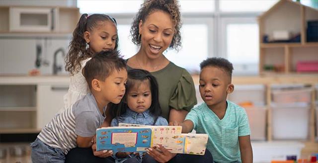Teacher reads while four students gather around her.
