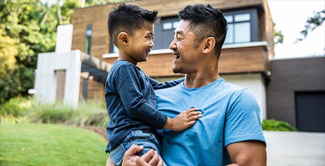 father holding son in front of modern house