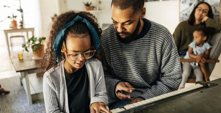Father teaching his daughter to play the piano for their family.