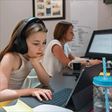 Young girl with earphones looking at notebook computer