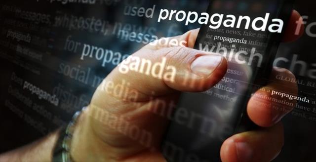 person holding a smartphone with the word propaganda across screen