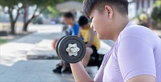 Teenage boy doing exercise with dumbbells in outdoor park