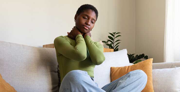 A woman sitting on a couch and holding her neck, illustrating common discomfort associated with overwork