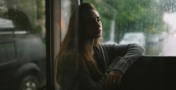 somber woman sitting at a window on a rainy overcast day.