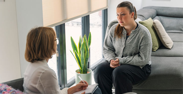 This image shows a cozy, modern living space where a person appears to be engaged in a serious discussion, likely related to mental health support