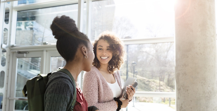Two teenage or young adult women walking down a hallway basking in sunlight.