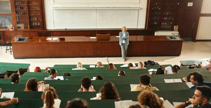 Professor standing at the front of a desk and students seated in a lecture hall