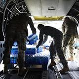 Uniformed personnel unload cases of bottled water from a cargo plane.