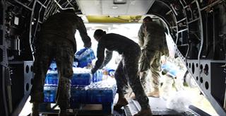 Uniformed personnel unload cases of bottled water from a cargo plane.