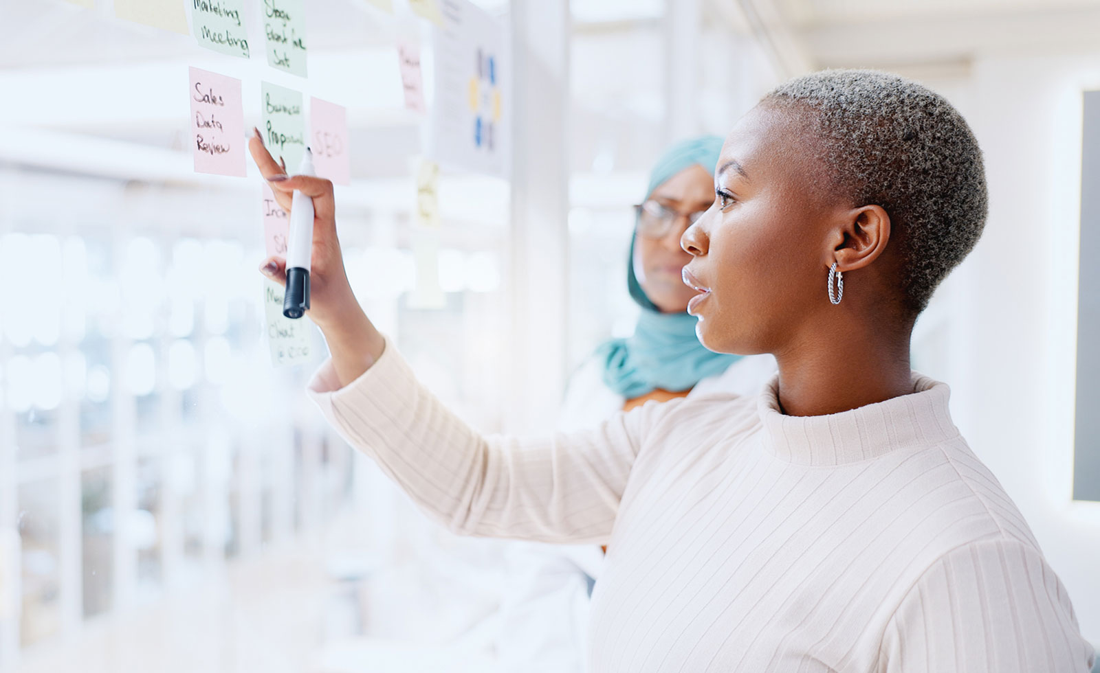Two female colleagues brainstorm ideas written on a glass wall.
