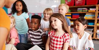 group of elementary school students sitting on floor listening to female teacher read story