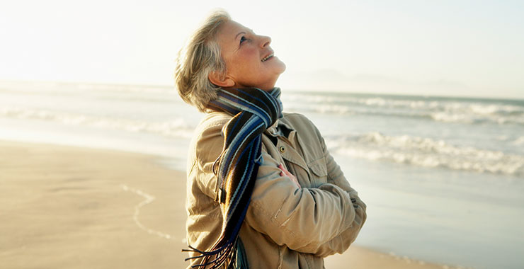 older woman on a beach looking up at the sky