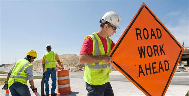 workers moving equipment and road signs on highway