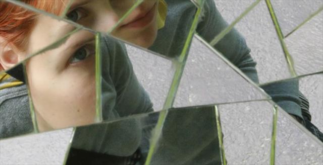 person’s face reflected in pieces of broken glass