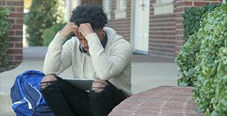 male college student rests head in hands while sitting on staircase