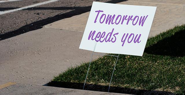 sign that reads "tomorrow needs you" placed by a sidewalk