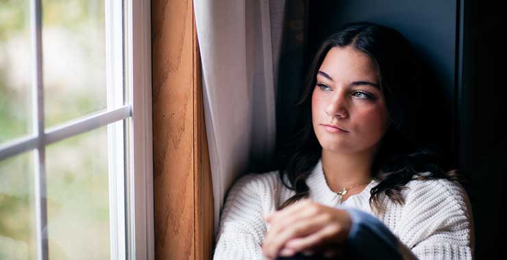 Young woman sitting near a window with a thoughtful and reflective expression