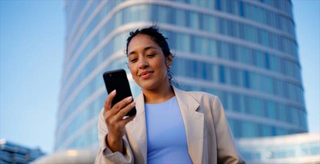 Smiling businesswoman using a smartphone in front of a sleek, modern office building